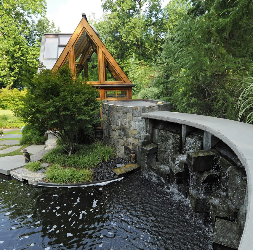 a weeping wall style waterfall drips into a koi pond
