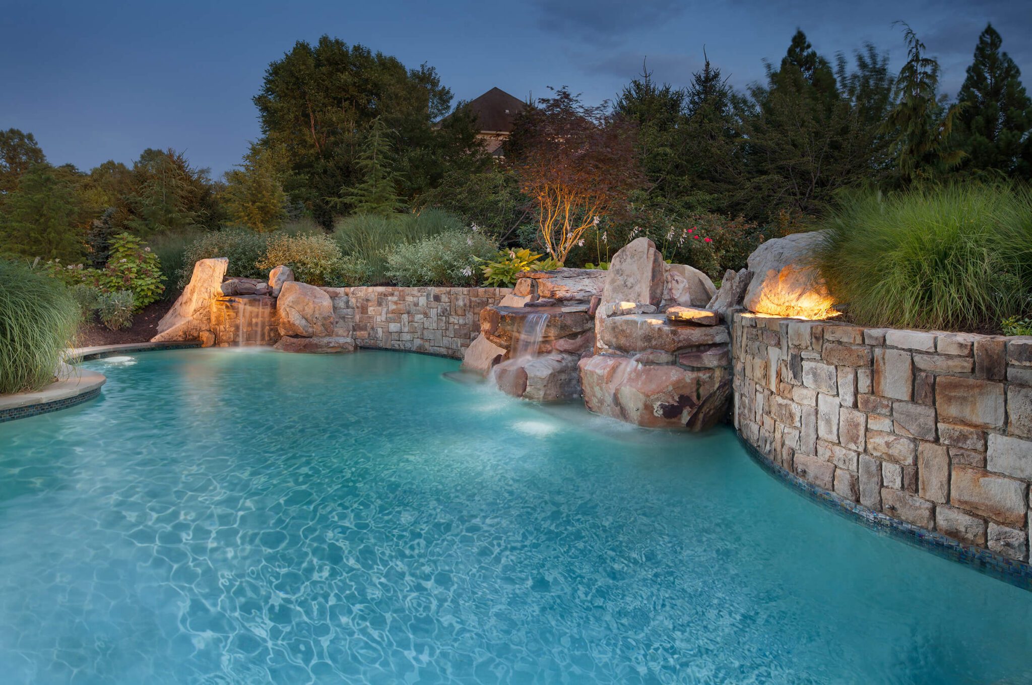 pool waterfalls pours over boulders and stone retaining wall