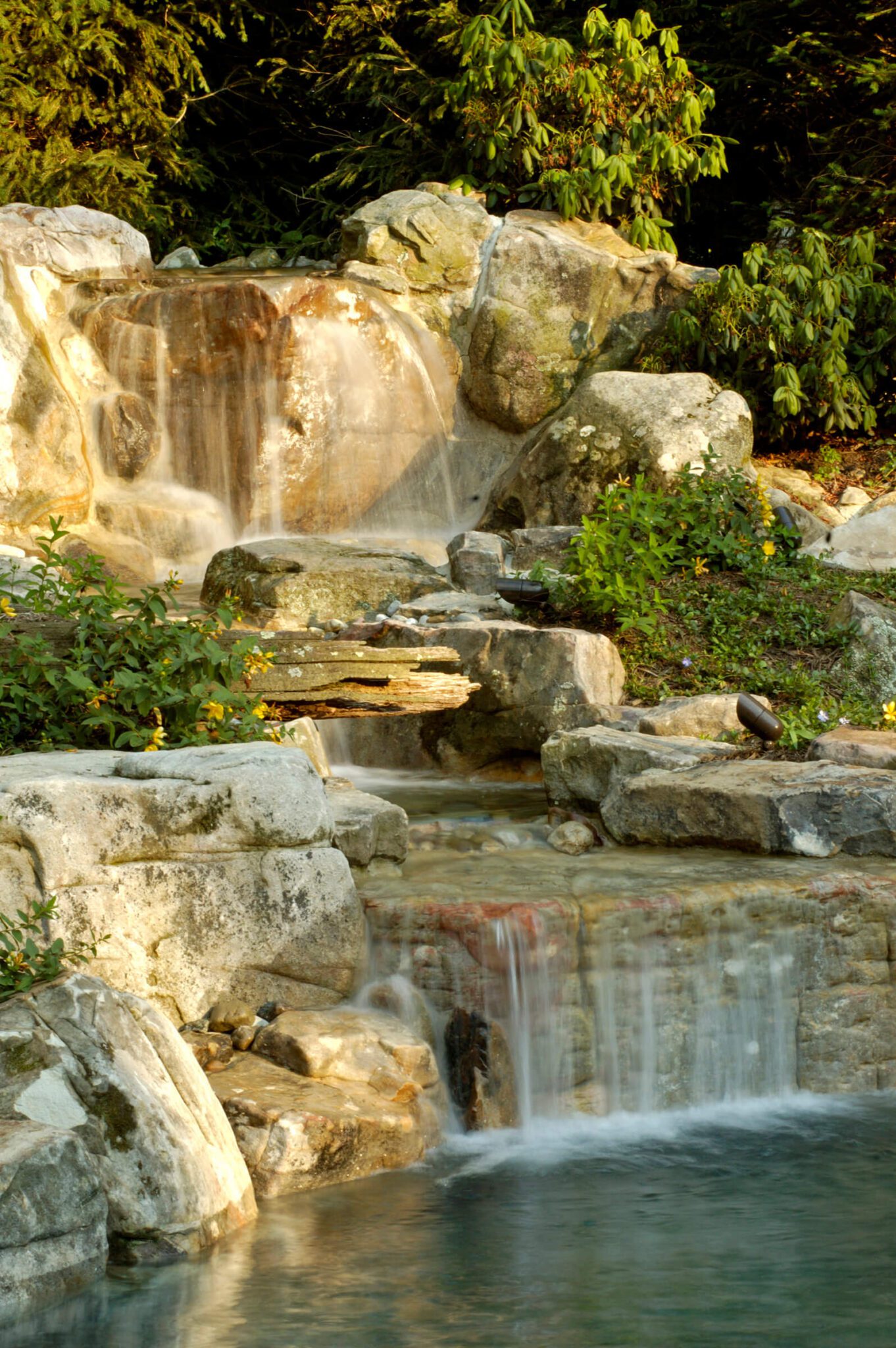 a tall multi-tiered waterfall spills into a backyard pond