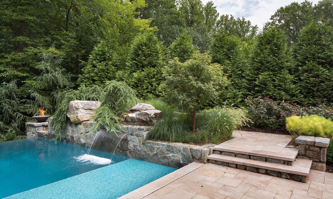 modern style zero edge swimming pool design with water feature and submerged sunbathing ledge
