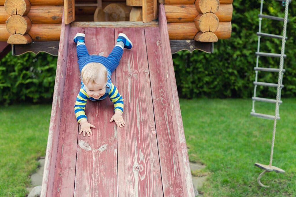 toddler going down a slide on backyard playhouse